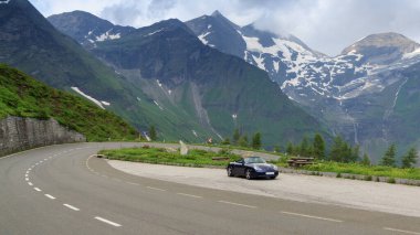 Fusch, Avusturya - 25 Temmuz 2021: Blue Roadster Porsche Boxster 986, Grossglockner High Alpine Road 'da dağ manzaralı ve virajlı. Araba Porsche tarafından üretilen bir spor arabadır..