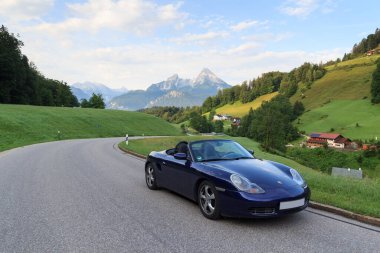 Berchtesgaden, Almanya - 25 Temmuz 2021: Mavi Roadster Porsche Boxster 986, Watzmann dağı ve sis panoraması. Araba, Porsche tarafından üretilen iki koltuklu orta-motorlu bir spor araba..