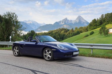 Berchtesgaden, Almanya - 25 Temmuz 2021: Mavi Roadster Porsche Boxster 986, Watzmann dağı ve sis panoraması. Araba, Porsche tarafından üretilen iki koltuklu orta-motorlu bir spor araba..