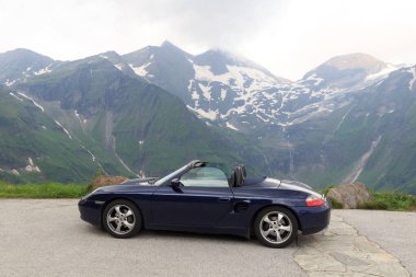 Fusch, Austria - July 25, 2021: Blue roadster Porsche Boxster 986 with mountain panorama at Grossglockner High Alpine Road. The car is a mid-engine two-seater sports car manufactured by Porsche.