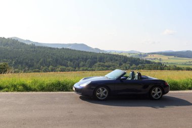 Gersfeld, Almanya - 23 Temmuz 2021: Mavi Roadster Porsche Boxster 986 ve Rhoen Dağları Panoraması. Araba, Porsche tarafından üretilen iki koltuklu orta-motorlu bir spor araba..