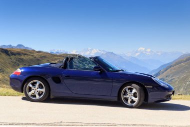 Realp, İsviçre - 13 Ağustos 2022: Blue Roadster Porsche Boxster 986 ve Furka Geçidi yolunda Dom ve Weisshorn dağlı panorama. Araba, Porsche tarafından üretilen orta-motorlu bir spor arabadır..