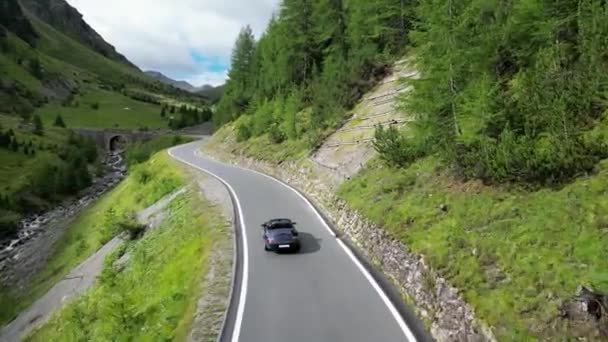 2023年7月30日 瑞士圣玛丽亚 蓝色保时捷911敞篷车驶上乌姆布拉伊尔山口 Umbrail Pass Road 上的一座石桥 走向高山阿尔卑斯山全景 这辆车是保时捷生产的跑车 — 图库视频影像