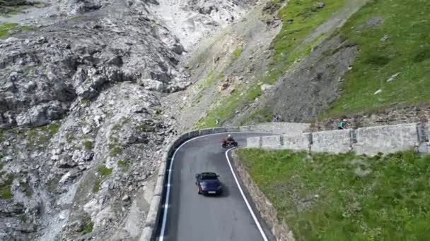 意大利斯蒂尔夫 2023年7月30日 一辆蓝色保时捷911敞篷车在史黛尔维奥山口路上驶上了山丘 一条与高山阿尔卑斯山全景相映成趣的蛇 超过了一个骑自行车的人 这辆车是保时捷生产的跑车 — 图库视频影像