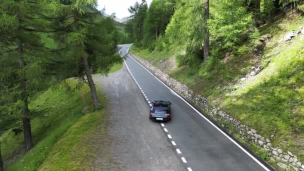 瑞士圣玛利亚 2023年7月30日 蓝色保时捷911敞篷车在Umbrail Pass路靠近树木的地方驶向高山阿尔卑斯山全景 这辆车是保时捷生产的跑车 — 图库视频影像
