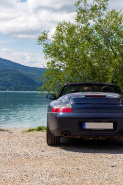 Kochel, Almanya - 29 Temmuz 2023: Mavi Porsche 911 üstü açık otopark Kochelsee Gölü ve Bavyera 'daki dağ alpleri manzarasının yanında.