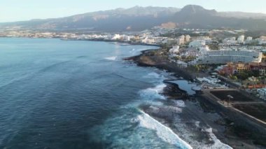 İspanya 'nın Kanarya Adası Tenerife' de güneş doğarken Atlantik Okyanusu üzerinde Costa Adeje ve volkan teide 'ye doğru Playa de las Americas otellerinin yanındaki panorama uçuşu