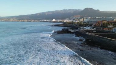 İspanya 'nın Kanarya Adası Tenerife' de güneş doğarken Atlantik Okyanusu üzerinde Costa Adeje ve volkan teide 'ye doğru Playa de las Americas otellerinin yanındaki panorama uçuşu