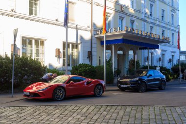 Lindau, Almanya - 10 Ağustos 2024: Ferrari ve Porsche lüks otomobiller Hotel Bayerischer Hof 'un önünde park ediyorlar. Bir turist Ferrari 'yi araştırıyor..