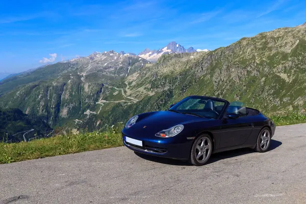 Realp, İsviçre - 11 Ağustos 2024: Mavi Porsche 911 üstü açık Furka Geçidi yolu ve dağ Finsteraarhorn ve İsviçre Alpleri 'ndeki Grimsel Geçidi yolu ile panorama.