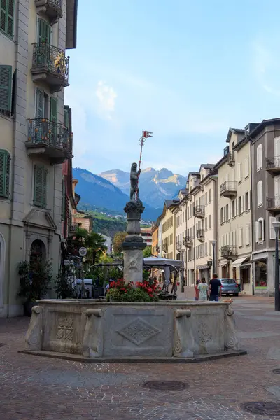Sion, İsviçre - 11 Ağustos 2024: Eski Sion kasabasında arka planda dağ manzarası olan yaya bölgesi, dükkan ve çeşme. Sion, İsviçre 'nin Valais kantonunun merkezi kent..