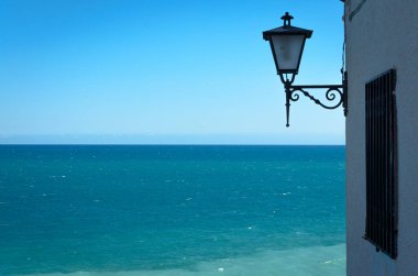 Arka planda turkuaz deniz suyu olan bir duvarda lamba, Peniscola, Castellon, İspanya