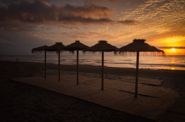 Sahildeki şemsiyeler arasında renkli bir gün batımı