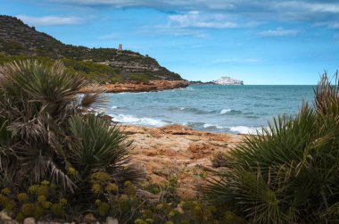 Sierra de Irta 'da kayalık bir sahil şeridinde deniz dalgaları. Arka planda Peniscola, Castellon, İspanya
