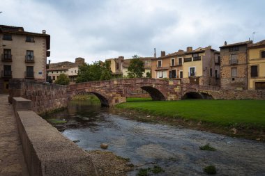 Kırmızı taş bloklardan yapılmış bir ortaçağ köprüsü manzarası ve bulutlu bir günde evlerin arkasındaki tepenin üstündeki şato Molina de Aragon, Guadalajara, İspanya