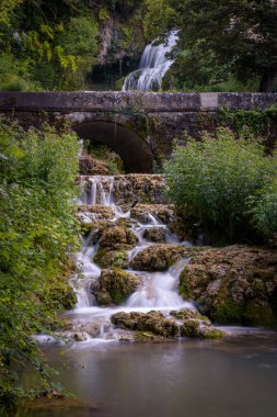 Small waterfall among the vegetation pouring water into a lake, Orbaneja del Castillo, Burgos, Spain