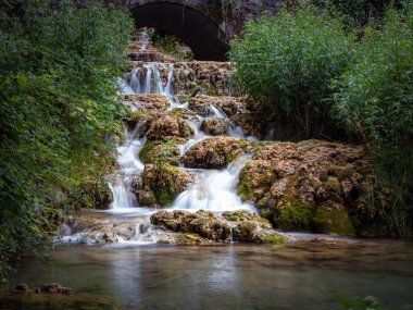 Small waterfall among the vegetation pouring water into a lake, Orbaneja del Castillo, Burgos, Spain