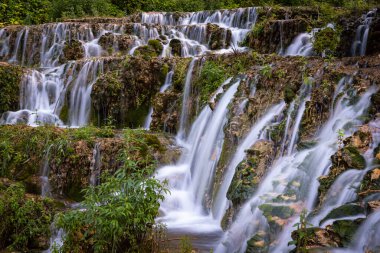 Small waterfall among the vegetation pouring water into a lake, Orbaneja del Castillo, Burgos, Spain