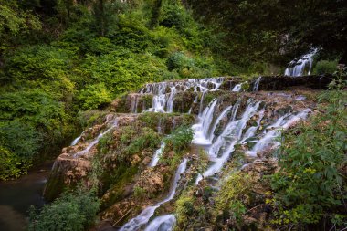 Small waterfall among the vegetation pouring water into a lake, Orbaneja del Castillo, Burgos, Spain