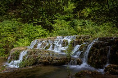 Small waterfall among the vegetation pouring water into a lake, Orbaneja del Castillo, Burgos, Spain