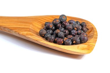 Beyaz arka planda tahta kaşıkta ardıç meyveleri