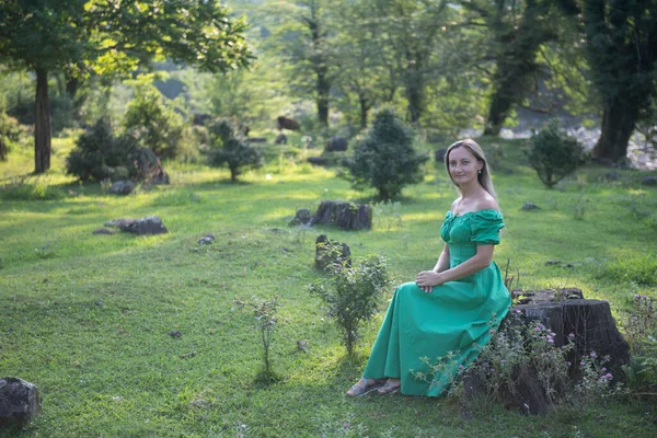 Yeşil elbiseli bir kız kütüğün üzerinde oturuyor. Yüksek kalite fotoğraf