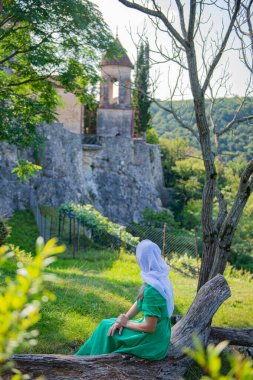 Yeşil elbiseli ve atkılı bir kız oturuyor ve manastıra bakıyor. Yüksek kalite fotoğraf