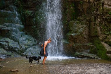 a girl in a blue dress and a black dog at a waterfall. High quality photo