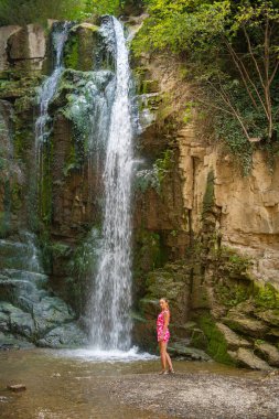 waterfall bridge one girl in pink dress stands. High quality photo