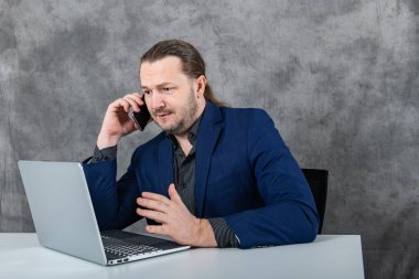 Bir adam dizüstü bilgisayarda çalışır ve telefonda konuşur. Yüksek kalite fotoğraf