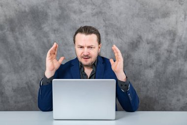 Gri arka planda dizüstü bilgisayarda çalışan üzgün bir işadamı. Yüksek kalite fotoğraf