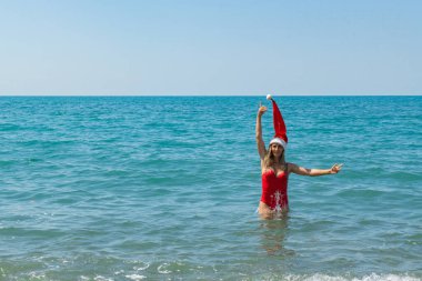 Deniz kenarında tatil eğlencesi: Kırmızı mayo ve Noel şapkalı kız. Yüksek kalite fotoğraf