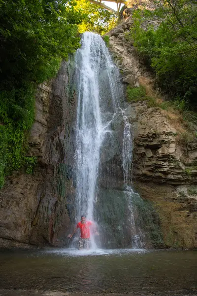 Dancing with the Falls: Man Captivated beneath the Waterfall. High quality photo