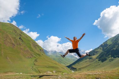 Dynamic Escape: Man in Orange T-Shirt Leaps Over Scenic Mountains. High quality photo