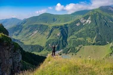 The lone figure in black clothing creates a striking contrast against the backdrop of a scenic mountain landscape and a captivating blue sky.