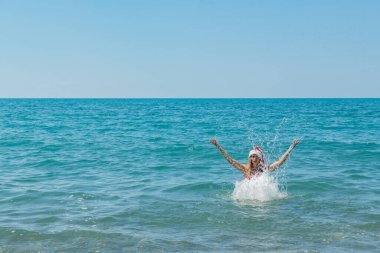 Plaj kenarı Santa Joy: Kırmızı mayo ve Noel Şapkalı kız. Yüksek kalite fotoğraf