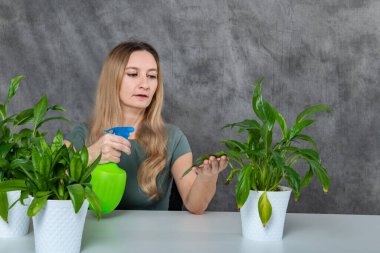 Masada oturan, sarı saçlı bir kız bu büyüleyici sahnede yeşil bitkilere fıskiyeyle bakıyor. Görüntü, canlı bitki yaşamına jest yapan kızları tasvir ediyor..