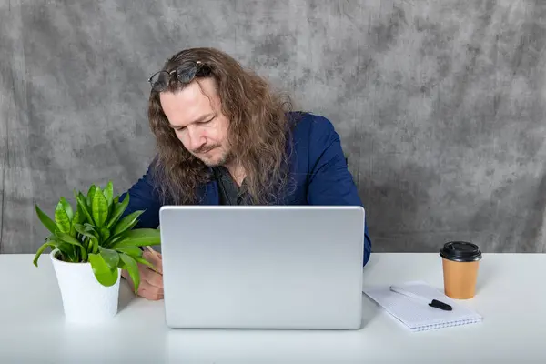 A dedicated young man with long hair is focused on his work as he types away on his laptop. The stylish and modern office setting creates a sleek backdrop for his professional endeavors.