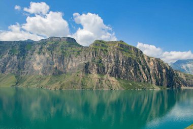 Yüksek tepeleri, dingin mavi gölü ve berrak mavi gökyüzü olan büyüleyici panoramik bir manzara. Tüm ihtişamıyla doğanın huzur verici ve ilham verici güzelliği..