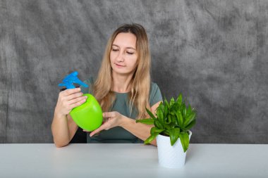 Sarı saçlı genç bir kız ahşap bir masada oturuyor, bir fıskiye kullanarak bir kaç canlı yeşil bitkiyi saksılarda sulıyor. Sahne, doğaya karşı bir bakım ve beslenme duygusu taşır..