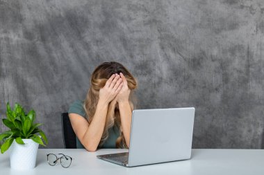 Altın rengi saçları ve zarif gri elbisesi olan zarif bir bayan dizüstü bilgisayarın yanında farklı pozlar veriyor. Canlı yeşil bir çiçek sahnenin güzelliğine renk katıyor..