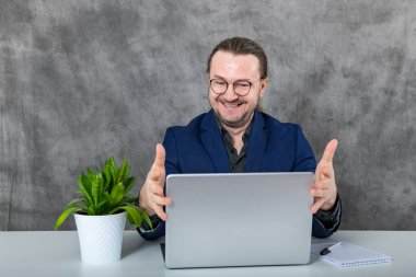 Mavi takım elbiseli ve gözlüklü zarif bir profesyonel modern ofis ortamında yemyeşil bir fabrikanın yanında çalışarak profesyonellik ve üretkenlik duygusunu aktarıyor..