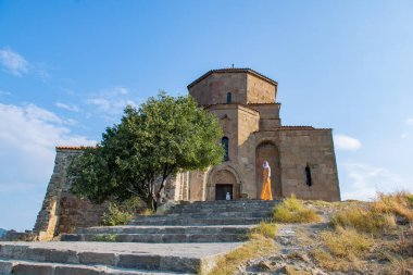 Canlı turuncu elbisesi ve beyaz atkısı olan şık, genç bir kadın zarif bir şekilde eski bir kilisenin önünde duruyor..