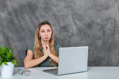 Şık gri elbiseli şık bir sarışın model dizüstü bilgisayarın yanında poz veriyor, canlı yeşil bir çiçek olay yerine renk katıyor, yaşam tarzı ve teknoloji kavramları için mükemmel..