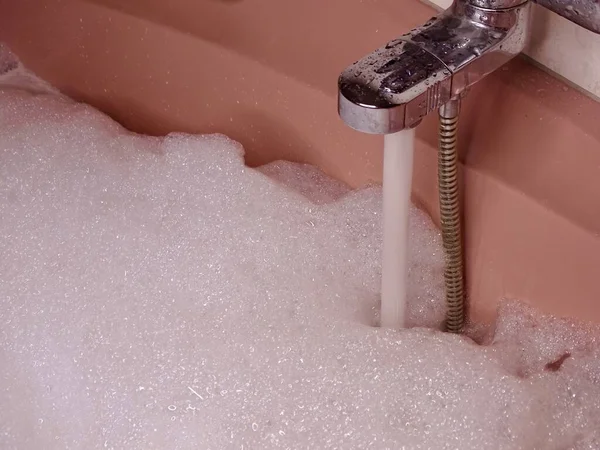 倒入边缘的粉红浴缸 充满水和丰富泡沫的金属水龙头 — 图库照片