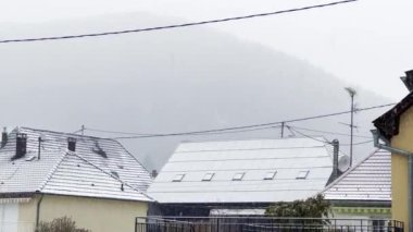 Banliyölerdeki Karlı Gün: Bir Dağ Arkaplanına Karşı Eklektik Çatılara Düşen Kar Taneleri Manzarası