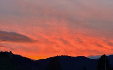 Siluetli Dağ Manzarası ve Çatıları Üzerinde Canlı Turuncu Bulutlarla Dramatik Günbatımı Gökyüzü