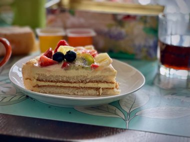 Arka planda ferahlatıcı bir içecek ile çiçekli bir tabakta lezzetli bir dilim meyveli sünger keki.