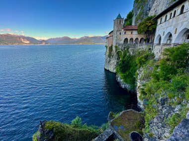 Santa Caterina del Sasso 'nun Maggiore Gölü' nün sakin sularına bakan kayalık yamaçtaki panoramik manzarası