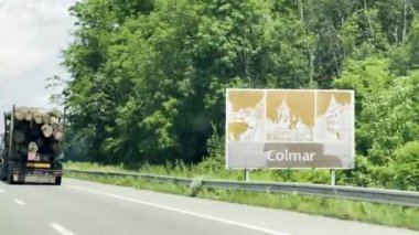 Colmar, Fransa - 6 Haziran 2024: Colmar, Alsace, Fransa 'ya doğru giden A35' in manzaralı karayolu manzarası, kütük taşıyan bir kamyon ve yemyeşil alanda bir Colmar hoş geldin tabelası